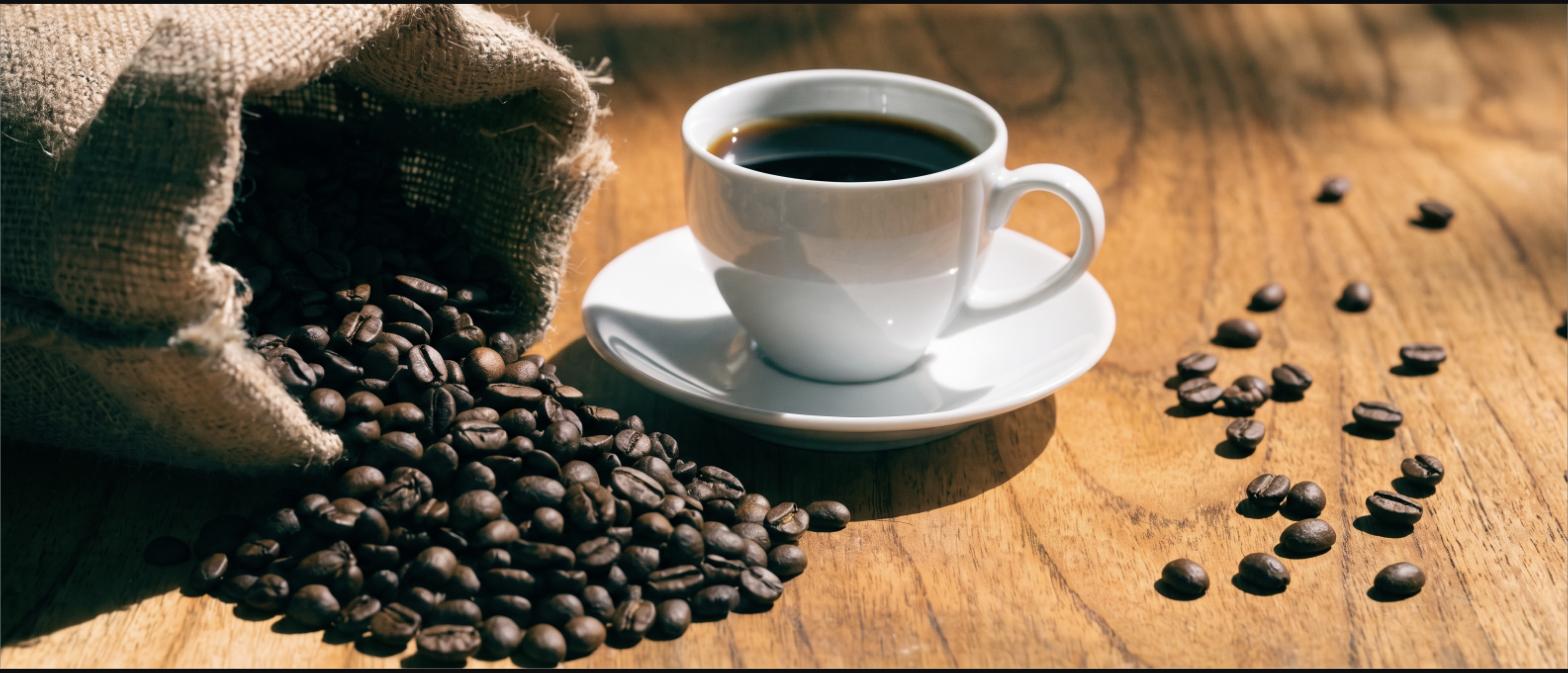 Roasted coffee beans spilling from a burlap sack beside a cup of black coffee